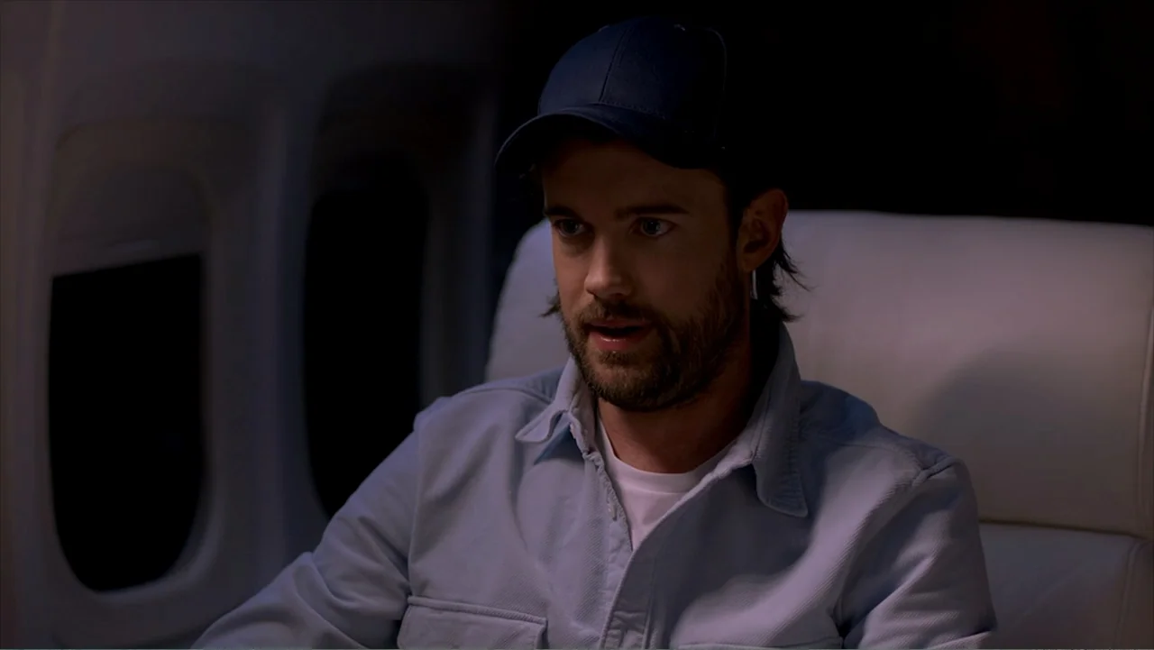 Jack in Time for Christmas (2024) movie still: medium — A dimly lit interior of an airplane cabin at night with a single passenger. The man sits in…