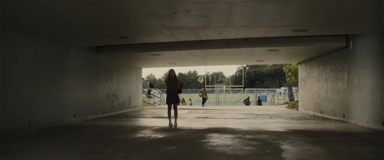 Afraid (2024) movie still: wide — A concrete underpass tunnels through to an outdoor athletic field with goalposts in distance. A solitary teenage…