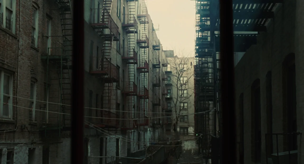Doubt (2008) movie still: establishing — A narrow, urban alleyway sits between two tall brick apartment buildings with fire escapes. Wires…