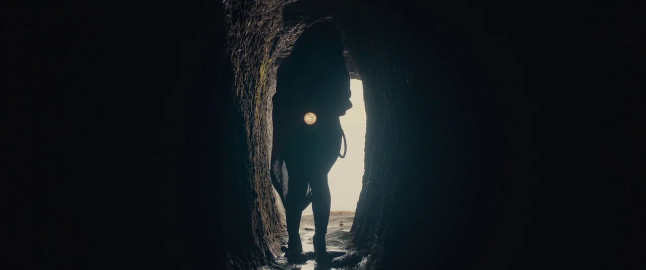 Kumiko the Treasure Hunter (2014) movie still: fullbody — A narrow damp stone tunnel with rough textured walls leads to a bright light source. A…