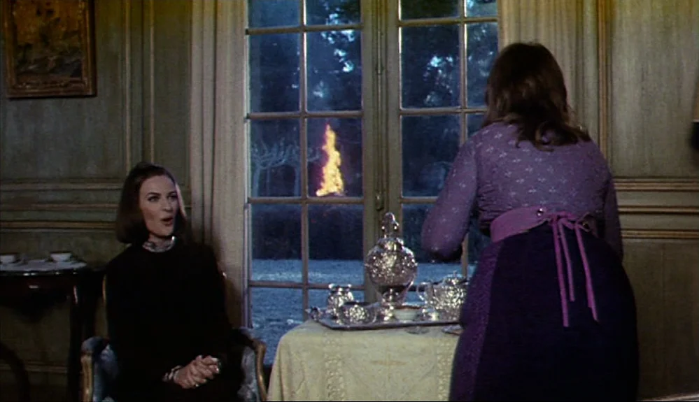 Harold and Maude (1971) movie still: medium — A refined room with wood-paneled walls features a tea service on a small table. Two women observe a…