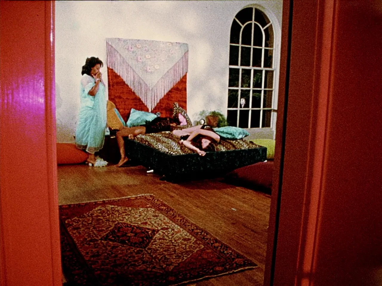 Space is the Place (1974) movie still: wide — A 1970s bedroom features a low platform bed with a leopard print cover. A woman stands on the hardwood…