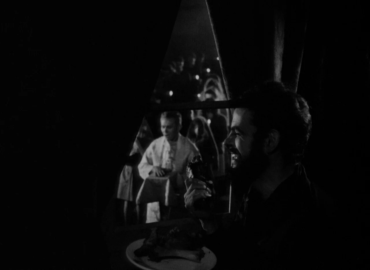 At Midnight I’ll Take Your Soul (1964) movie still: medium — A dark, dimly lit dining area frames a man eating in the foreground shadow. A second…