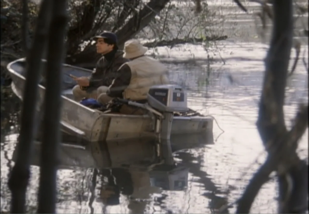 White Mile (1994) movie still: medium — Two men sit in a small aluminum boat floating on calm water near trees. The men hold fishing rods while the…