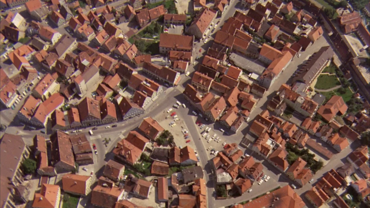 Willy Wonka & the Chocolate Factory (1971) movie still: establishing — A dense European townscape features interconnected buildings with steep…