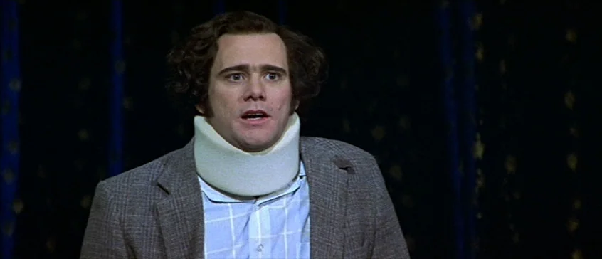 Man On The Moon (1999) movie still: medium — A man stands before a dark curtain backdrop in a dimly lit studio environment. The man wears a foam…