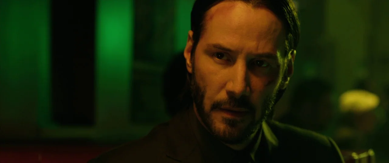 John Wick (2014) movie still: closeup — A dark indoor space filled with intense green neon ambient lighting. A man with a short beard and dark hair…
