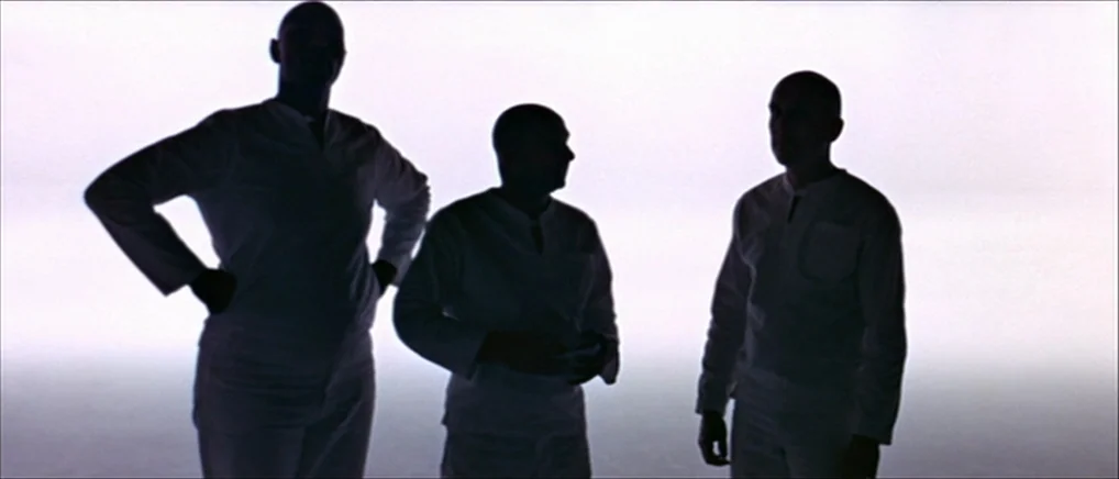THX 1138 (1971) movie still: fullbody — Three men stand in silhouette against a pure white background in a studio space. The subjects are arranged…