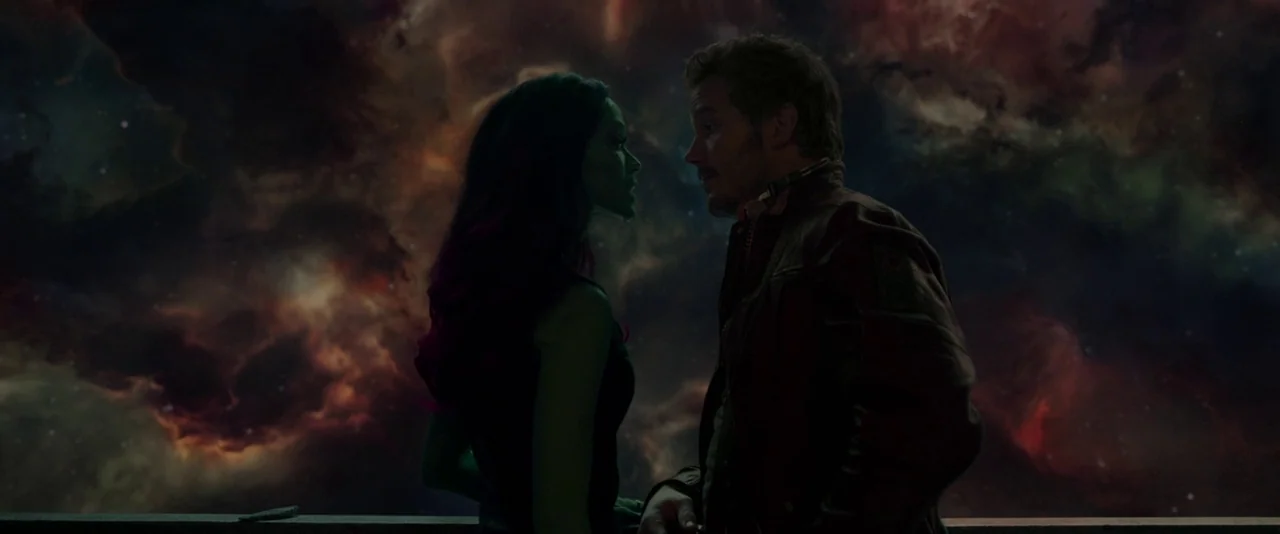 Guardians of the Galaxy (2014) movie still: medium — A man and a green-skinned woman stand on a ship deck overlooking space. A swirling, colorful…