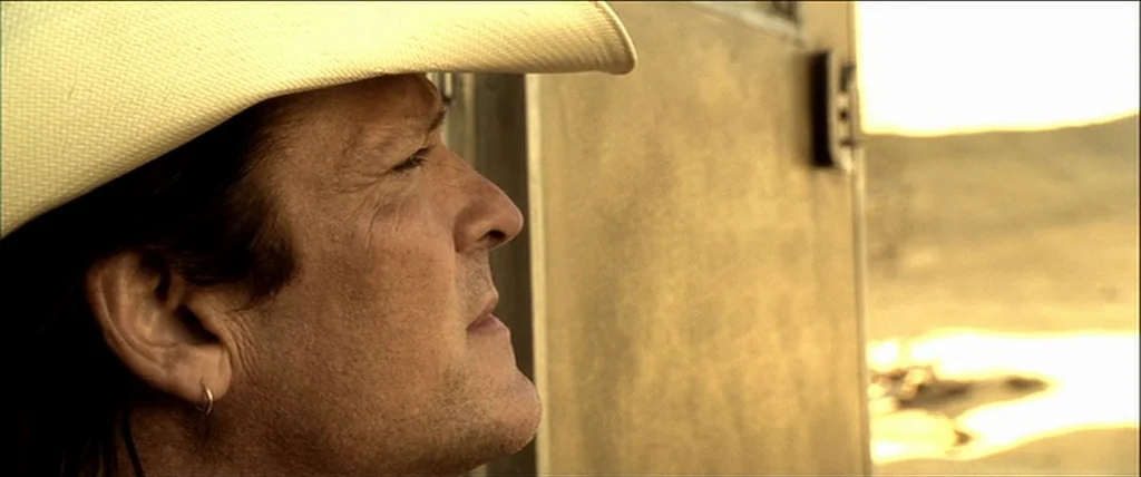 Kill Bill Vol. 1 (2004) movie still: closeup — A man in a light cowboy hat stands in an arid desert environment. He is positioned in side profile…
