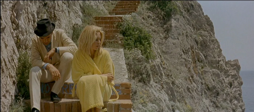 Contempt (Le Mépris) (1963) movie still: medium — A stone staircase carved into a rugged coastal cliff leads down toward the sea. A man in a light…