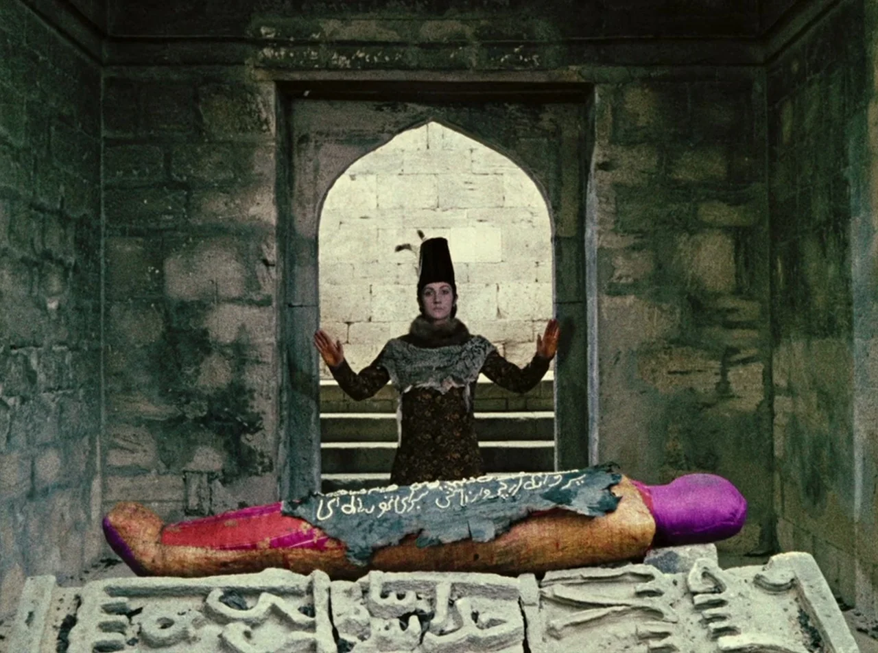 The Colour of Pomegranates (1969) movie still: fullbody — A stone vaulted tomb features a central archway leading to a staircase outside. A person…