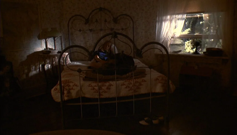 Badlands (1973) movie still: wide — A dimly lit room features a metal bed frame covered by a patterned quilt. A young girl sits on the mattress…