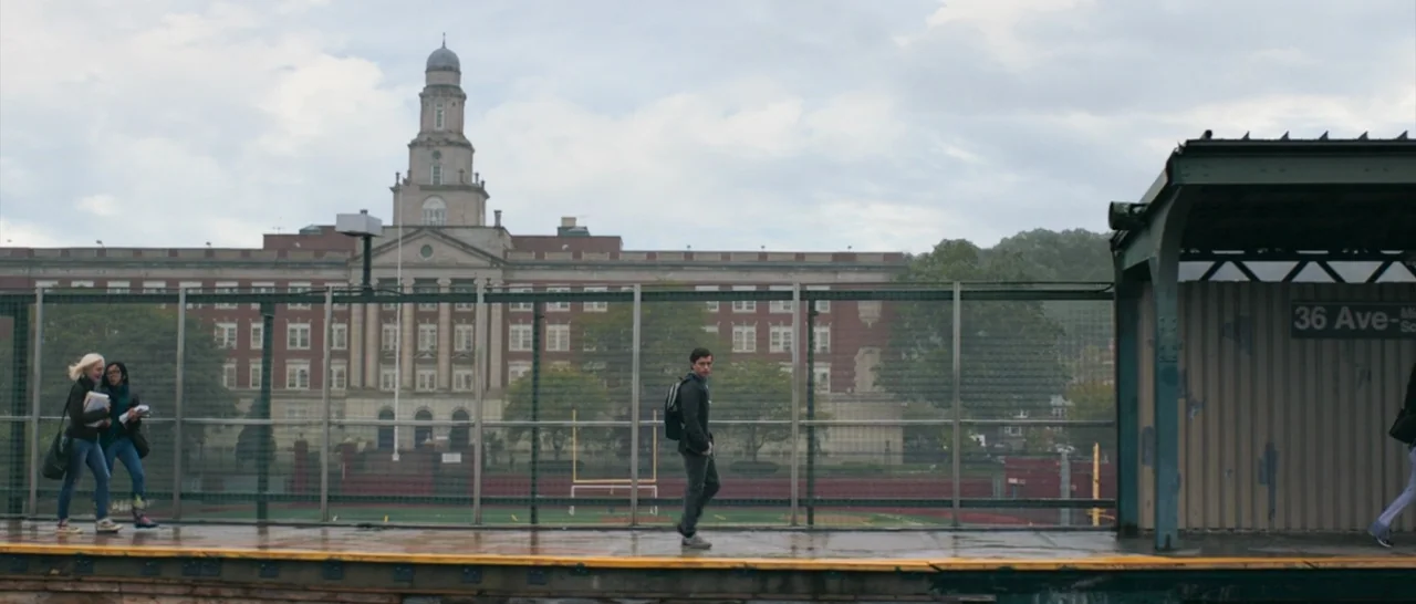 Spider Man: Homecoming (2017) movie still: wide — A suburban subway platform overlooks a brick high school building with a football field. A teenage…