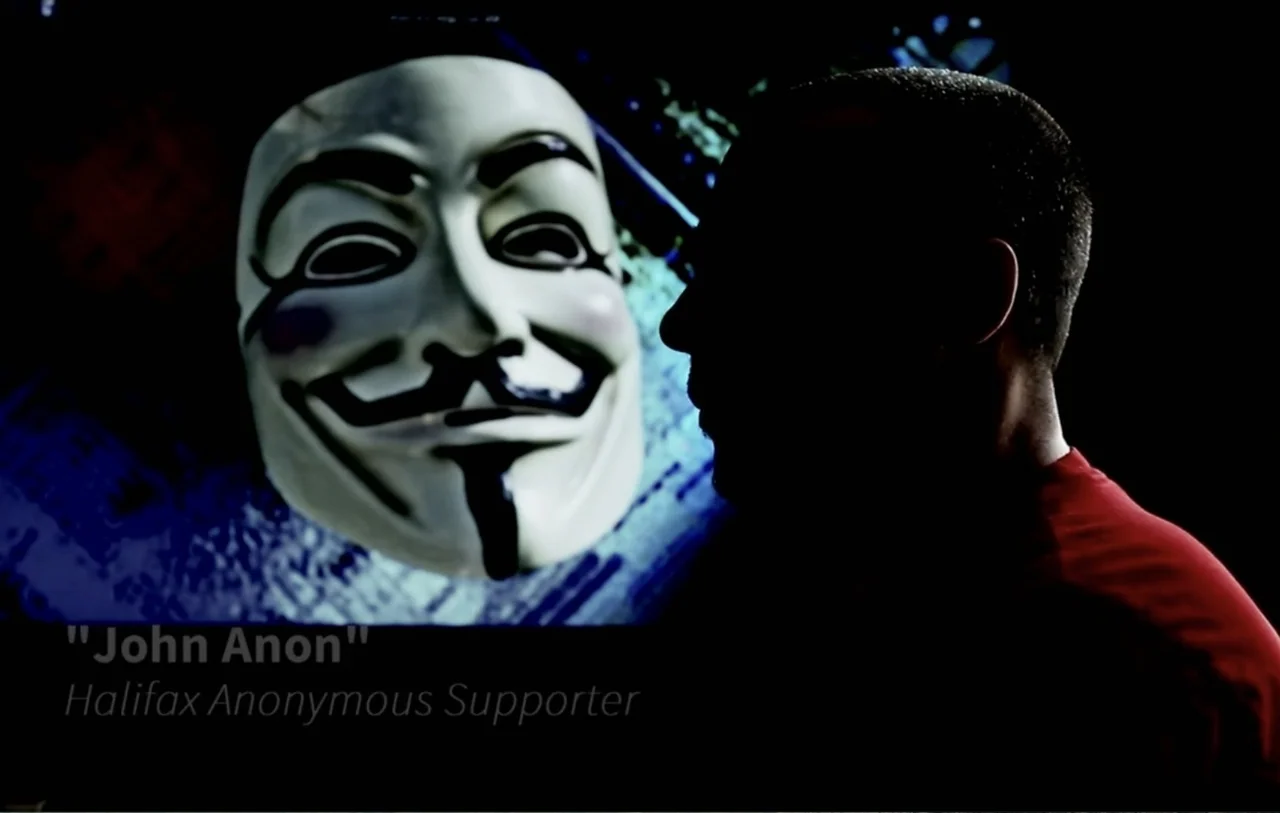 No Place to Hide (1992) movie still: medium — A dark space features a glowing screen displaying a white Guy Fawkes mask graphic. A person in profile…