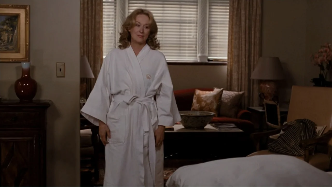 It's Complicated (2009) movie still: fullbody — A hotel room interior featuring beige walls, a window with blinds, and furniture. A middle-aged…