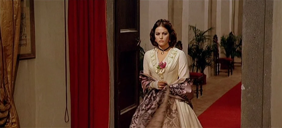 The Leopard (1963) movie still: medium — A historic manor hallway features a red carpet runners and interior potted plants. A woman in a period…