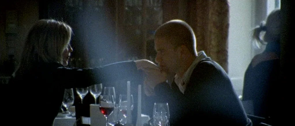 Reconstruction (2003) movie still: medium — A dimly lit restaurant table is cluttered with wine glasses and thin white candles. A woman reaches…