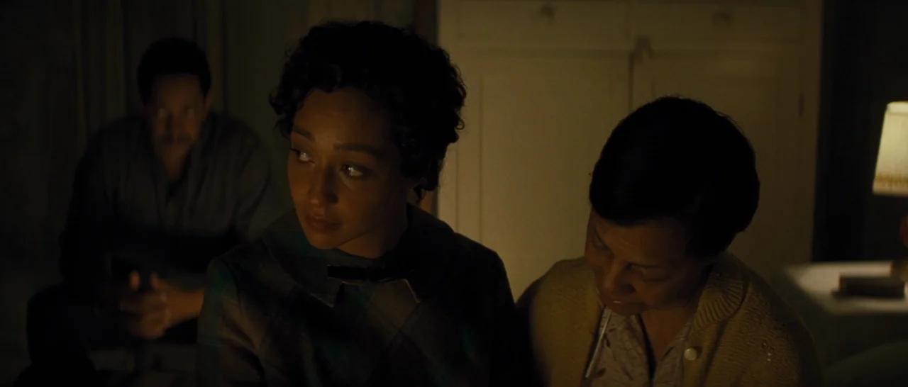 Loving (2016) movie still: medium — A dimly lit room at night features three people sitting together in darkness. The woman in the center looks to…
