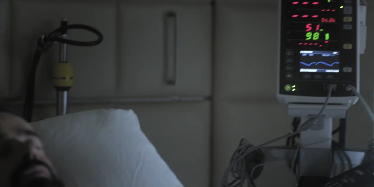 Stalked by My Doctor: A Sleepwalker's Nightmare (2019) movie still: closeup — A hospital room contains a patient lying in a bed next to a monitor. A…