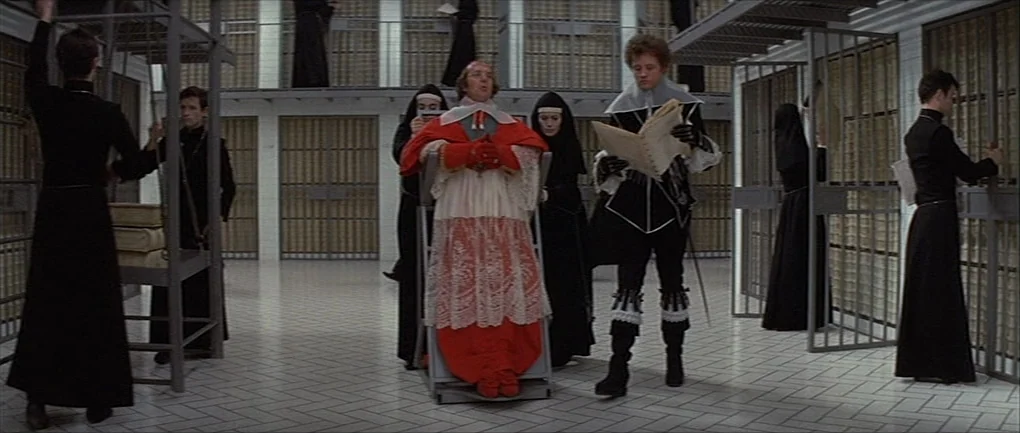 The Devils (1971) movie still: wide — A modern white-tiled prison block with metal grated partitions and multiple levels of catwalks. A central…