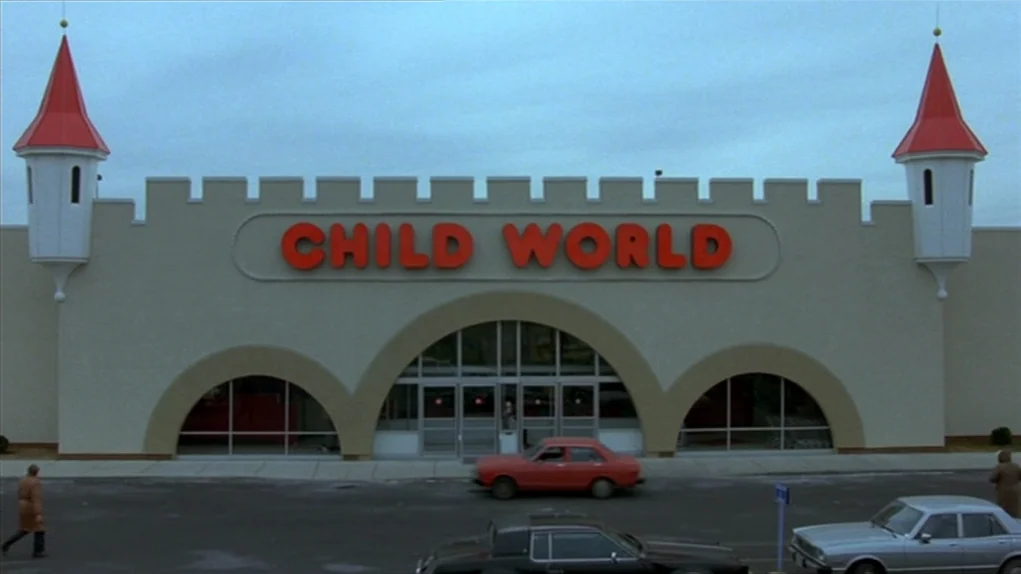 The Colour of Money (1986) movie still: wide — A toy store exterior features a castle-themed facade with twin red conical towers. A parking lot…