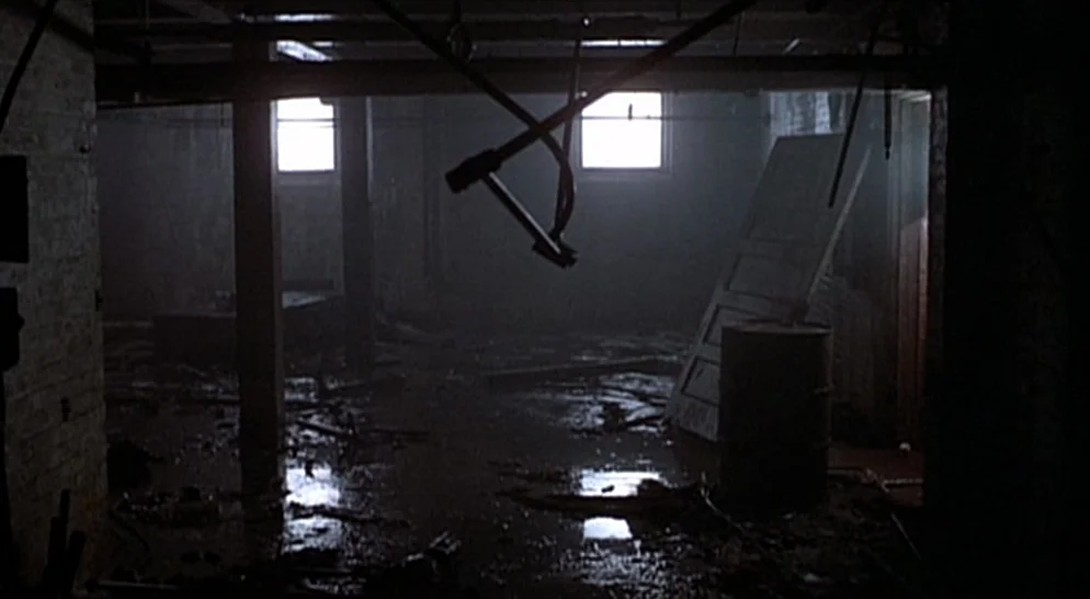 The French Connection (1971) movie still: establishing — A dark, unfinished basement with debris scattered across a wet, stained concrete floor. Two…