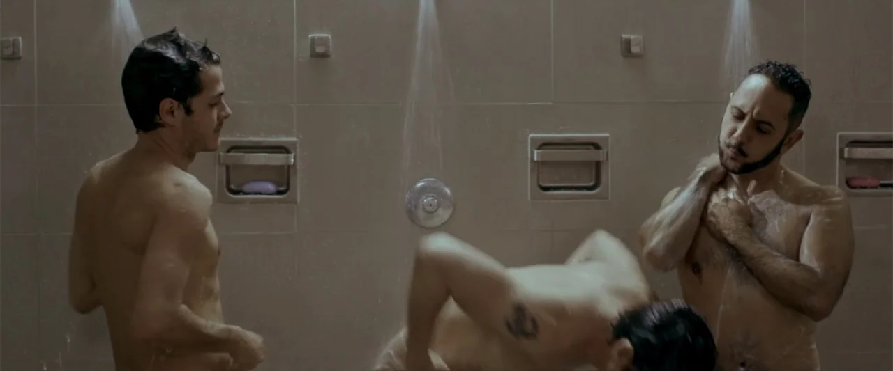 Do It Like An Hombre (2017) movie still: medium — A tiled communal facility with multiple shower heads and recessed wall soap dishes. Three men are…