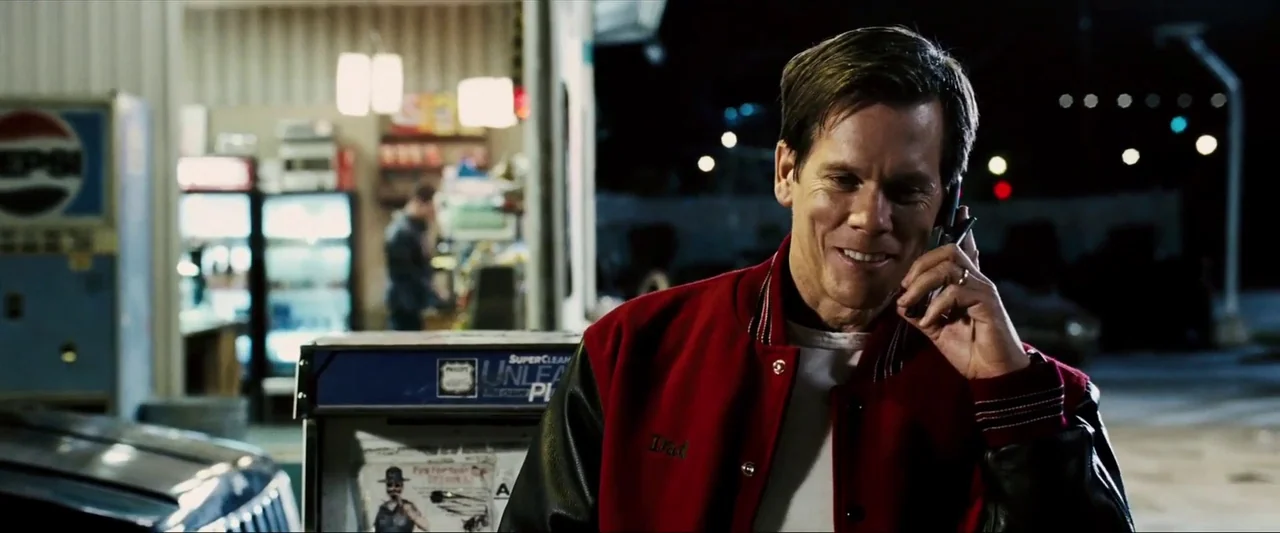Death Sentence (2007) movie still: medium — A man stands at a gas station pump at night with buildings visible behind. The man holds a mobile phone…