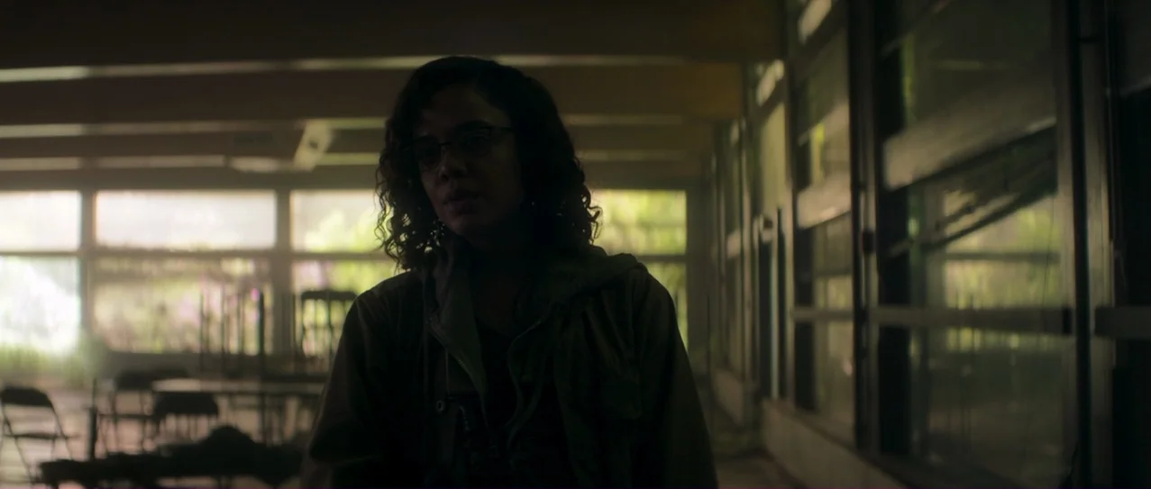Annihilation (2018) movie still: medium — A dimly lit industrial hallway features floor-to-ceiling windows along one side of the frame. A woman with…
