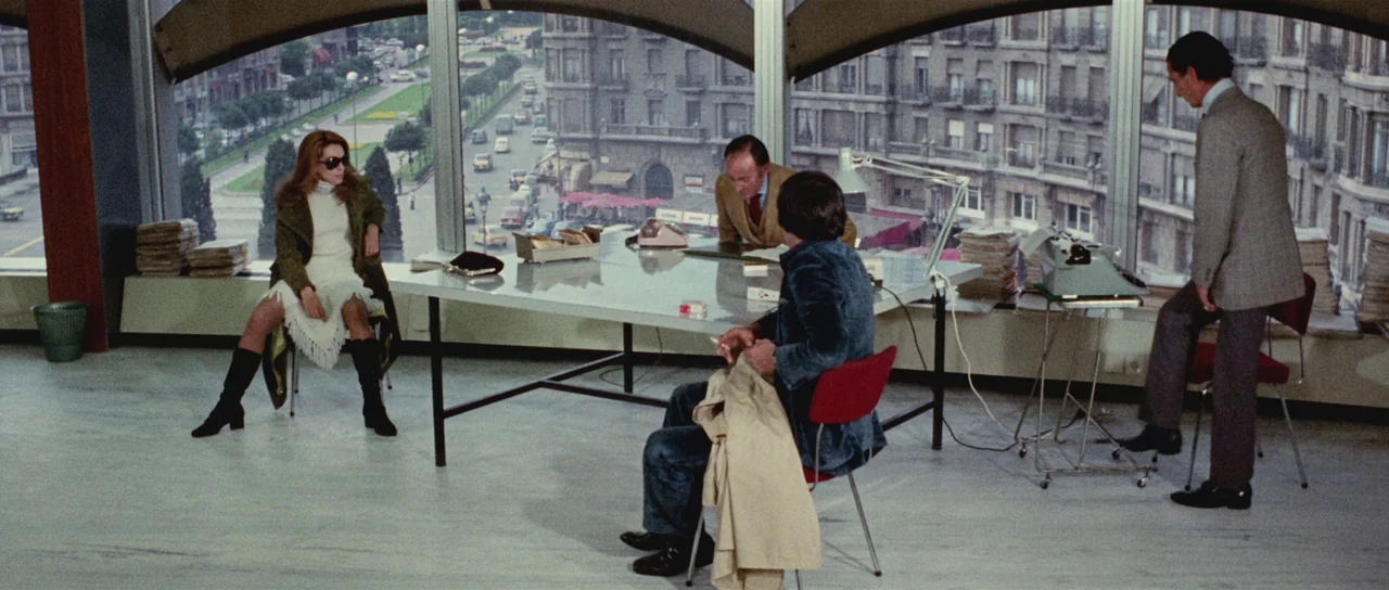 Death Walks On High Heels (1971) movie still: wide — A spacious office interior features panoramic curved windows overlooking a dense city street.…