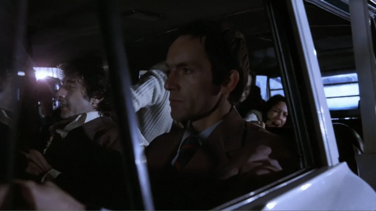 Dog Day Afternoon (1975) movie still: medium — The interior of a crowded passenger vehicle shows multiple people seated during daylight. A man in a…
