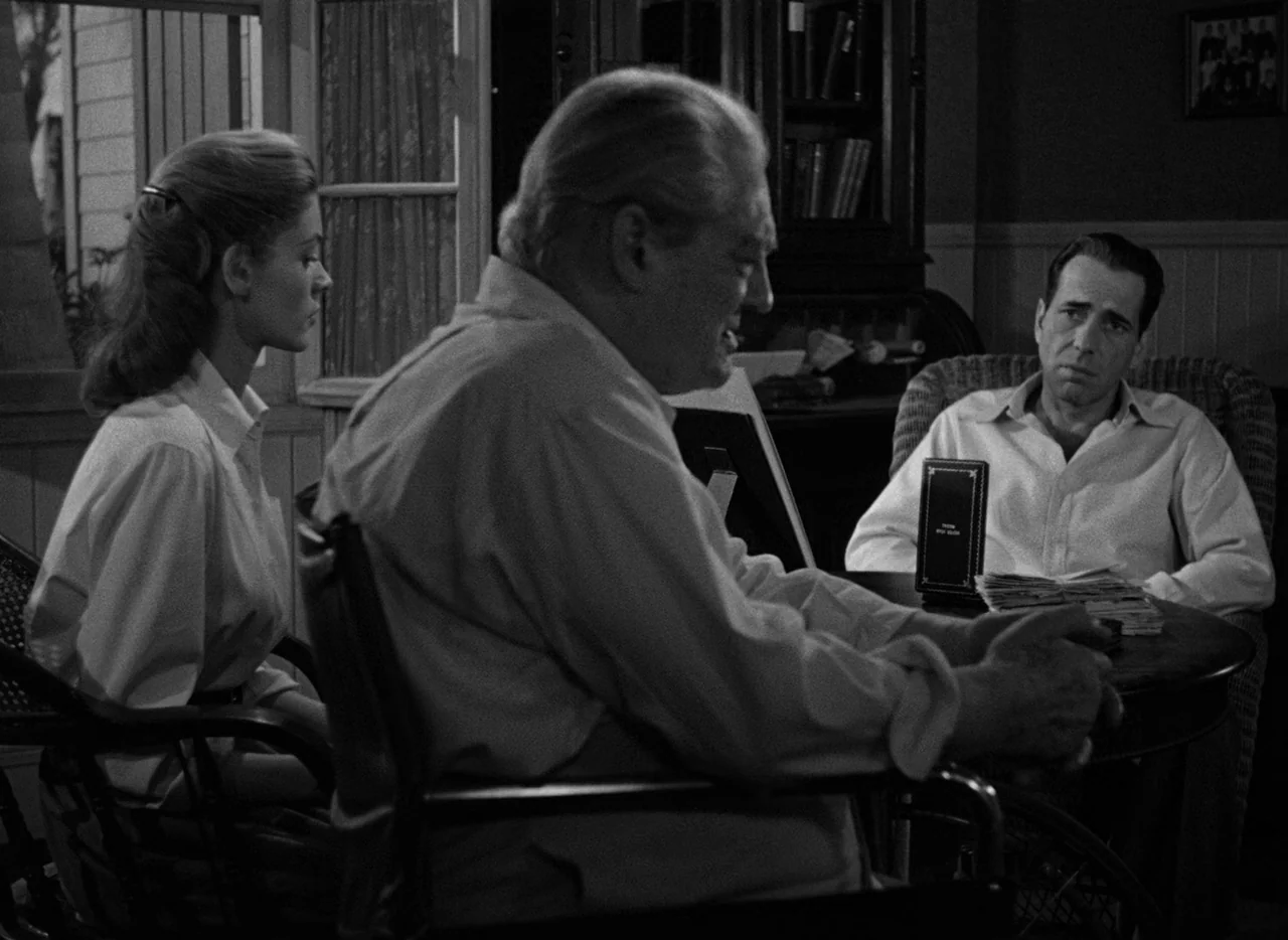 Key Largo (1948) movie still: medium — A wood-paneled room features a round table surrounded by three people in chairs. A glass door leads to a…