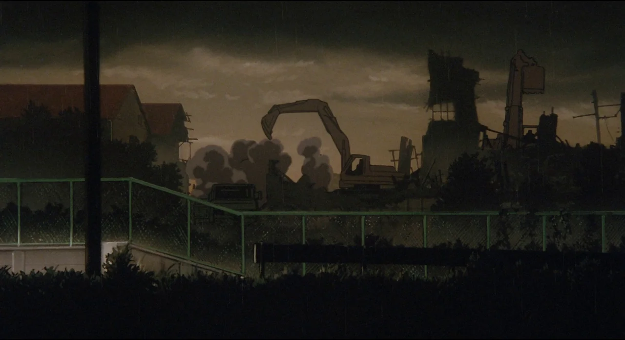 Millenium Actress (2001) movie still: wide — A dark, rainy construction site features heavy machinery operating among ruined buildings at dusk.…