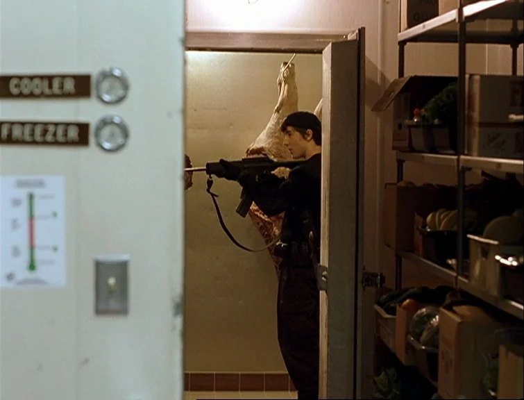 Elephant (2003) movie still: medium — A cramped industrial walk-in cooler contains metal shelving units and a hanging animal carcass. A young man…