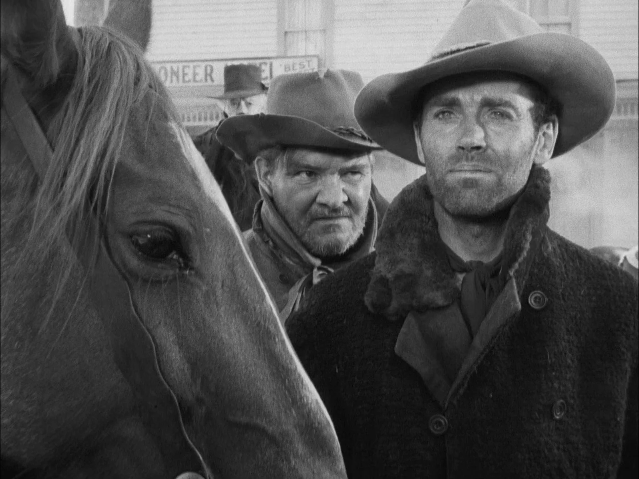 The Ox-Bow Incident (1942) movie still: medium — A dusty outdoor scene features two men standing near a horse in front of building. The background…