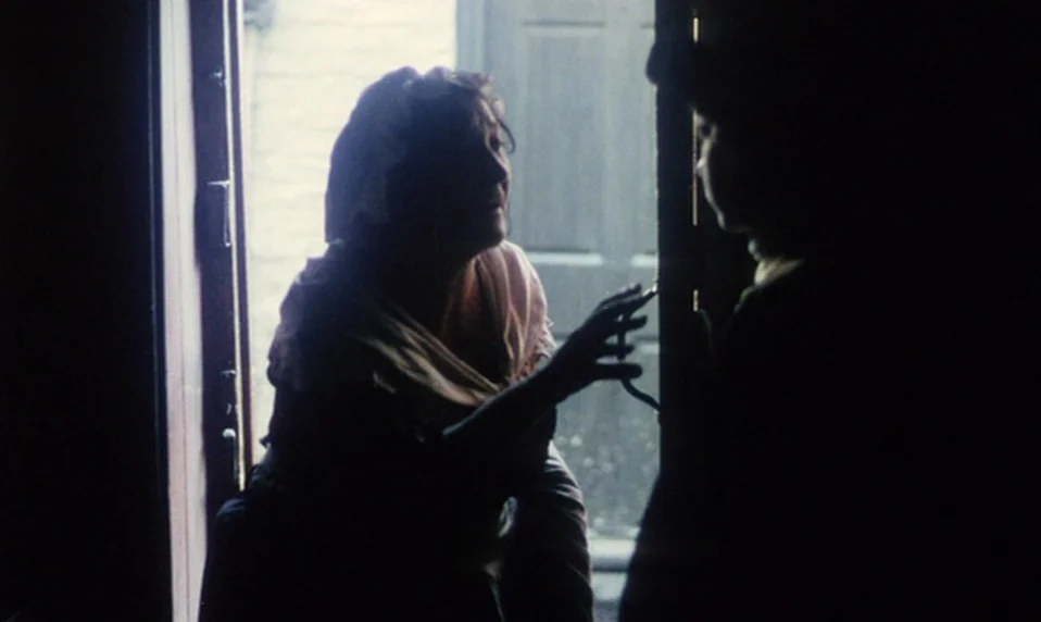 Black Jack (1979) movie still: medium — A dark, shadowed entryway frames a woman peering into a bright exterior space. She reaches out her hand…