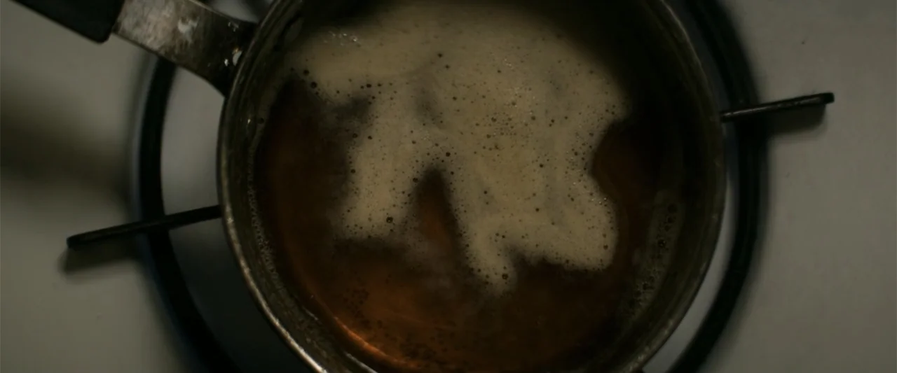 The Equalizer (2014) movie still: closeup — A metal saucepan sits on a white electric stove burner. Dark brown liquid bubbles gently within the…