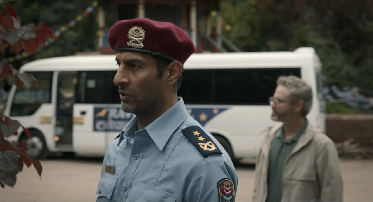 Ice Road: Vengeance (2025) movie still: medium — A gravel parking area features a white minibus parked in the soft daylight. A police officer in a…