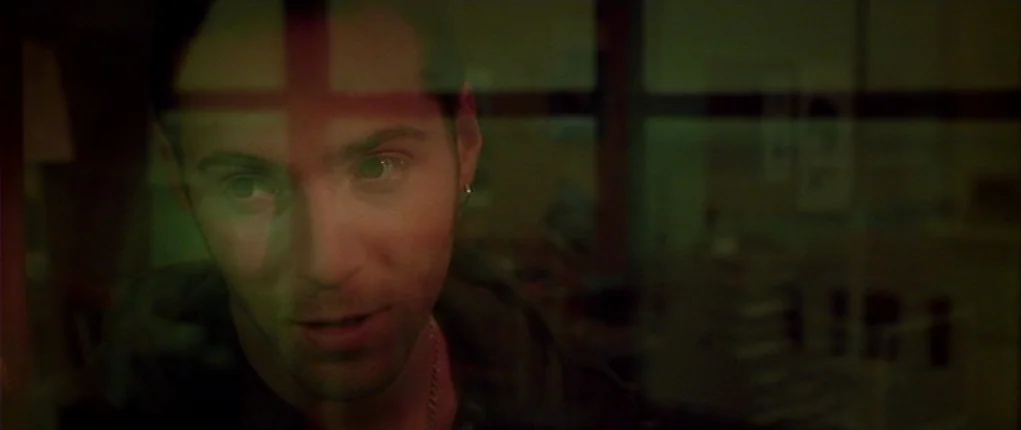 I Want You (1998) movie still: closeup — A dimly lit room seen through a pane of glass at night. A young man gazes through the glass with a red…
