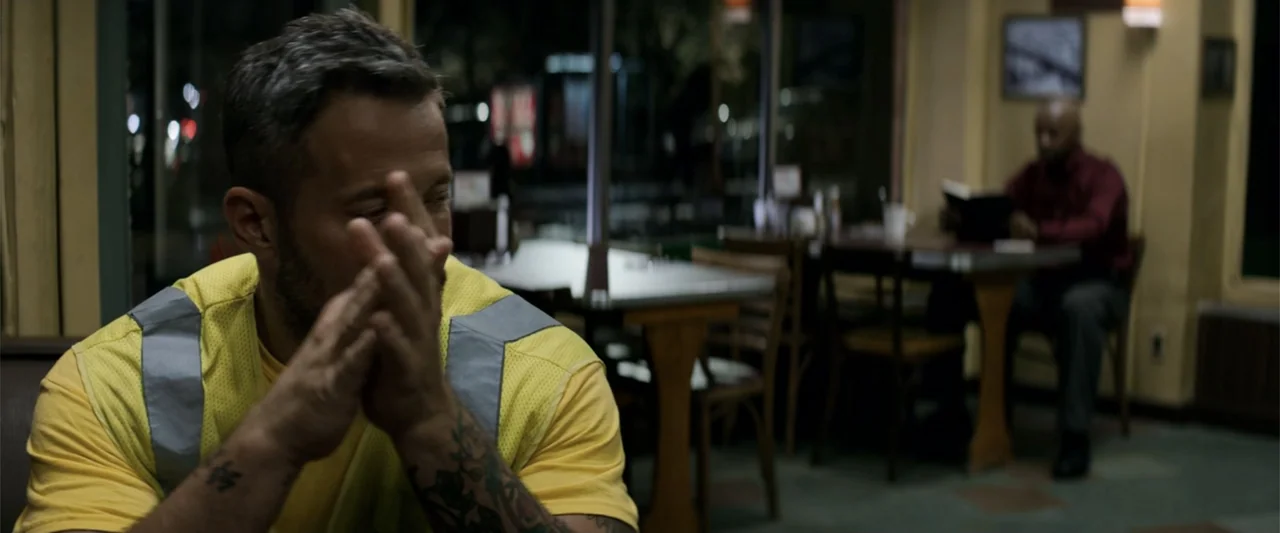 The Equalizer (2014) movie still: medium — A quiet diner interior with tables and chairs sits in darkness at night. A man in a high-visibility vest…