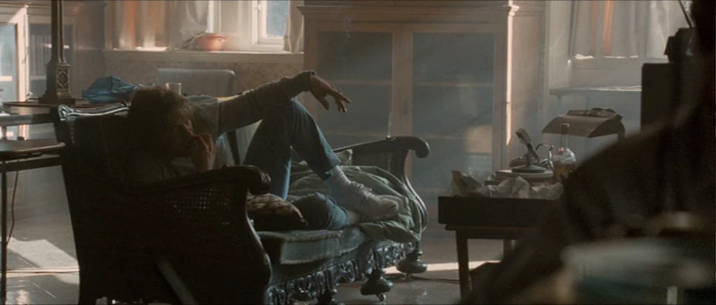 Tinker Tailor Soldier Spy (2011) movie still: medium — A cluttered living room features a wooden cabinet, window, and low wooden furniture. A young…