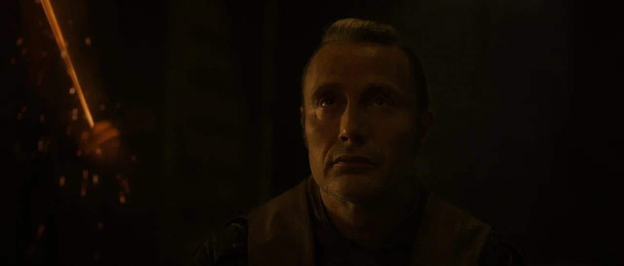 Doctor Strange (2016) movie still: closeup — A man stands in a dimly lit, nondescript interior space with deep shadows. The man gazes forward while…