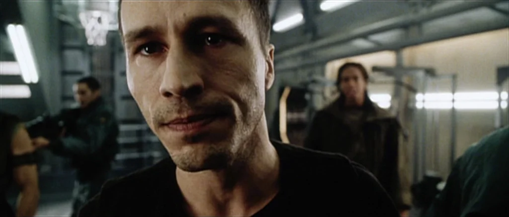 Alien: Resurrection (1997) movie still: closeup — An industrial-style training area with metal walls and bright overhead lighting fixtures. A man in…