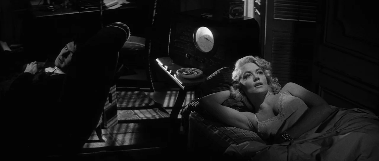 The Tarnished Angels (1957) movie still: medium — A dark living room contains a vintage radio with a glowing dial on a table. A blonde woman rests…