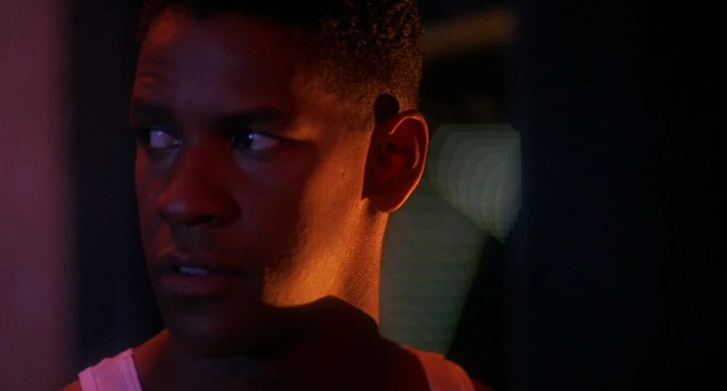 Mo’ Better Blues (1990) movie still: closeup — A dark interior space illuminated by distinct red neon lighting. A man looks sideways towards an…
