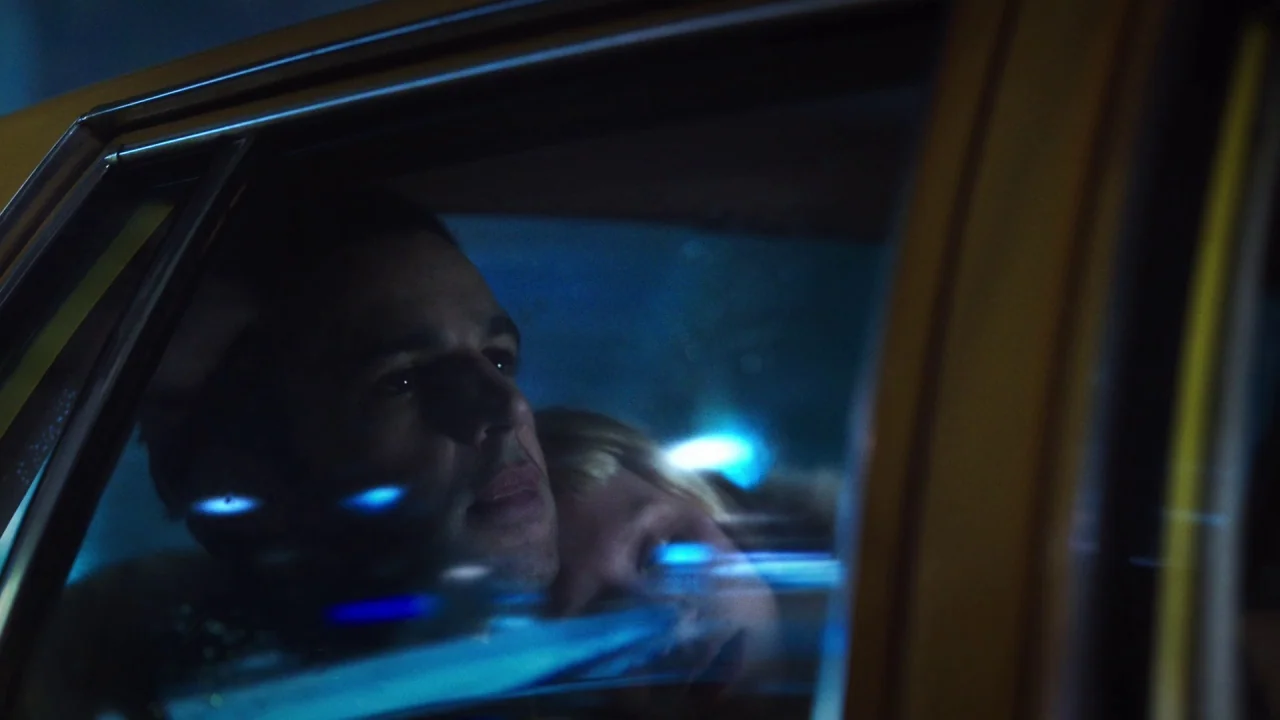 Piercing (2018) movie still: closeup — The interior of a moving taxi at night captures reflections on the side window. A man and a blonde woman are…