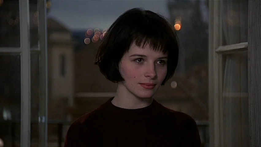 The Unbearable Lightness of Being (1988) movie still: closeup — A woman stands before an open door at night with city lights blurred behind her. She…