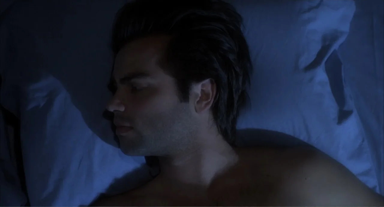 I, Madman (1989) movie still: closeup — A man lies on a pillow in a dimly lit, blue-tinted bedroom at night. The man rests on his side with his head…
