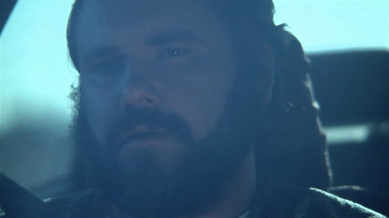 A Horrible Way To Die (2010) movie still: closeup — A man sits inside a vehicle with a view of a bright outdoor environment. He gazes forward while…